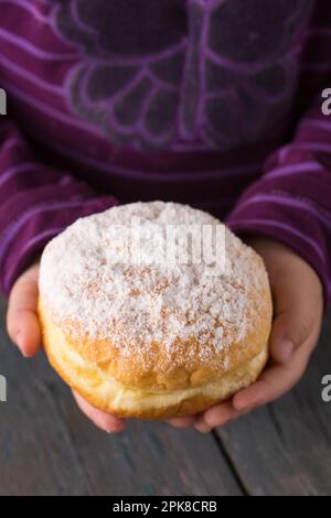 Ruddy délicieux beignets berliners avec remplissage arrosé dans les mains des enfants Banque D'Images