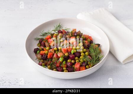Vinaigrette à salade de légumes avec betteraves, pommes de terre, carottes, cornichons, pois verts et herbes dans une assiette blanche sur fond bleu clair. Russe traditionnel Banque D'Images