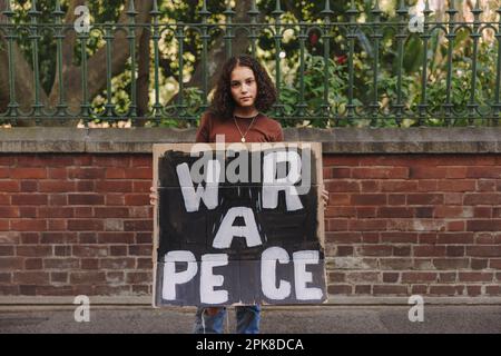 Un jeune militant de la paix regarde la caméra tout en tenant une affiche anti-guerre. Adolescent protestant contre la guerre et la violence. Banque D'Images