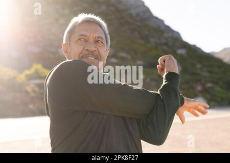 Heureux homme biracial senior portant des vêtements de sport, s'étendant sur la rue dans les montagnes Banque D'Images