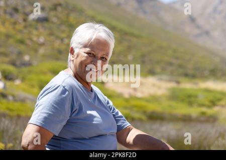 Portrait d'une heureuse femme biraciale senior regardant l'appareil photo et souriant dans les montagnes Banque D'Images