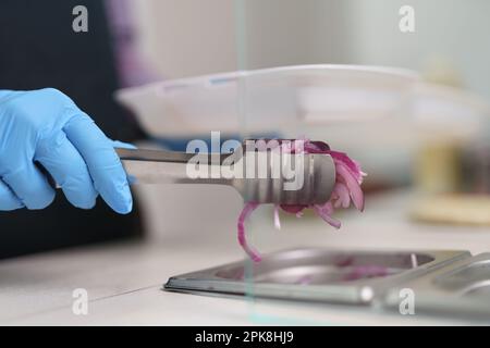 Cuire prend des oignons rouges tranchés avec des pinces dans un récipient dans la cuisine Banque D'Images