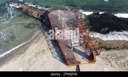 Ancienne jetée en bois avec des gens qui se reposent et vieux brise-lames en béton sur la plage de sable de la rive de la mer par une journée ensoleillée. Plage publique. Côte de mer, littoral de mer. Paysage côtier. Vue de dessus. Vue aérienne de drone Banque D'Images