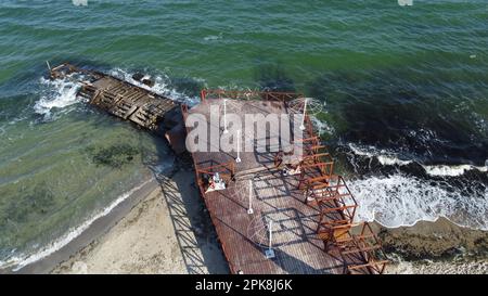 Ancienne jetée en bois avec des gens qui se reposent et vieux brise-lames en béton sur la plage de sable de la rive de la mer par une journée ensoleillée. Plage publique. Côte de mer, littoral de mer. Paysage côtier. Vue de dessus. Vue aérienne de drone Banque D'Images