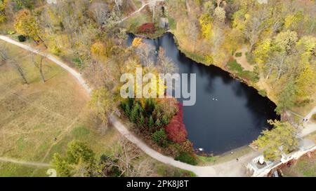 Magnifique vue sur un parc d'automne avec des arbres avec des feuilles mortes jaunes, des lacs, de l'architecture, des clairières et des personnes marchant le long des chemins de terre le jour de l'automne. Vol au-dessus du parc d'automne. Vue de dessus. Banque D'Images