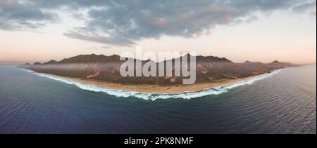 Vue d'en haut, vue panoramique sur la plage de Cofete entourée par la chaîne de montagnes du Parc naturel de Jandía pendant un beau coucher de soleil. Banque D'Images