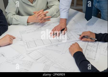 Un homme du caucase est debout pour apporter des changements à un dessin, trois collègues sont assis à une table et l'écoutent. Banque D'Images