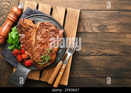 Steaks de l'os en T. Tranché de bœuf grillé en T-bone ou steak de viande de portreuse avec épices romarin et poivre sur un panneau de marbre noir sur fond de bois ancien. À Banque D'Images