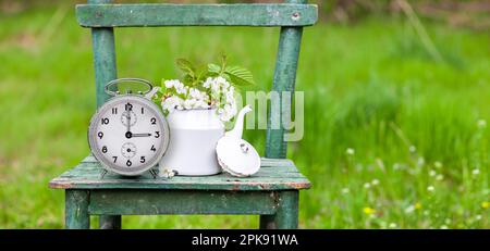 Chaise, bouquet de fleurs, réveil, cadran d'horloge avec trois horloges, symbole de changement d'heure à l'heure d'été Banque D'Images