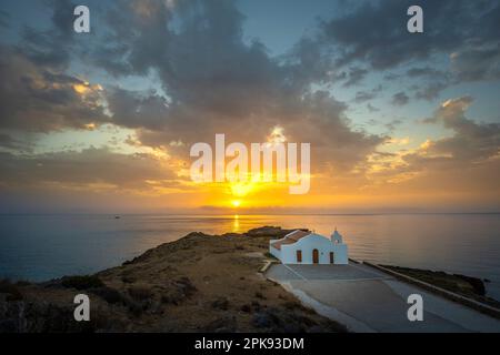 Petite église grecque typique juste au bord de la mer, la chapelle blanche d'Agios Nikolaos sur une côte rocheuse au lever du soleil Banque D'Images