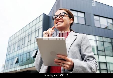Femme designer freelance tenant la tablette numérique entre les mains et souriant, pensée positive, rêvant de réaliser un projet d'entreprise réussi. Banque D'Images