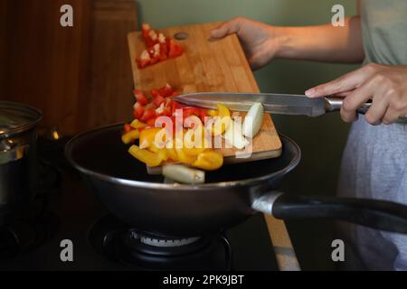 Femme mettant des légumes coupés dans une poêle dans la cuisine, gros plan Banque D'Images