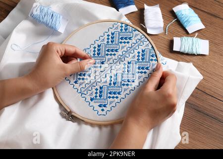 Femme brodant une chemise blanche avec fil bleu sur une table en bois, vue ci-dessus. Vêtements nationaux ukrainiens Banque D'Images