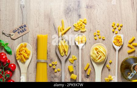 cuillères en bois avec différents types de pâtes, tomates, huile et sans gluten Banque D'Images