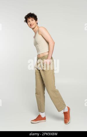 insouciante bigote dans le débardeur et les baskets posant avec la main dans la poche de pantalon beige sur fond gris, image de stock Banque D'Images