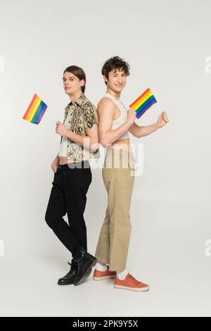 pleine longueur de modèles pansexués stylés posant avec de petits drapeaux lgbt sur fond gris, image de stock Banque D'Images