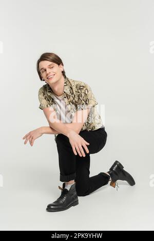 pleine longueur de gaie modèle non binaire en pantalon noir et blouse à imprimé animal regardant loin sur fond gris, image de stock Banque D'Images