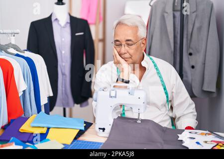 Homme d'âge moyen avec coiffeur de cheveux gris utilisant la machine à coudre pensant fatigué et ennuyé avec des problèmes de dépression avec les bras croisés. Banque D'Images