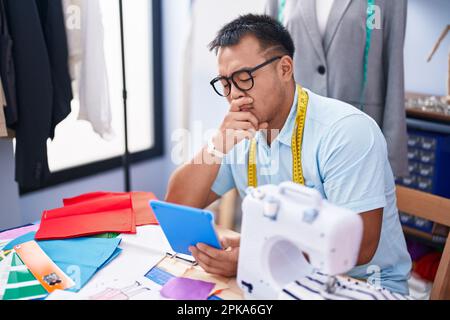 Jeune homme chinois tailleur utilisant le pavé tactile avec une expression sérieuse dans la boutique de tailleur Banque D'Images