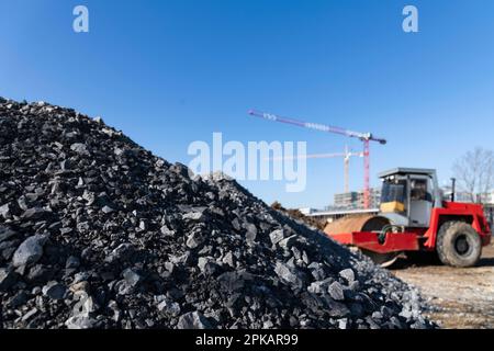 Le rouleau rouge se trouve sur un grand chantier de construction devant des monticules de gravier avec des grues de construction en arrière-plan Banque D'Images