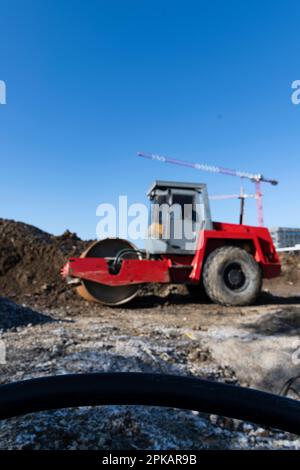 Le rouleau rouge se trouve sur un grand chantier de construction devant une pile de terre avec des grues de construction en arrière-plan Banque D'Images