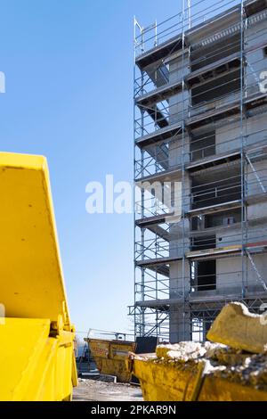 Conteneur jaune pour les supports de déchets de construction devant une coque d'échafaudage à ciel bleu Banque D'Images