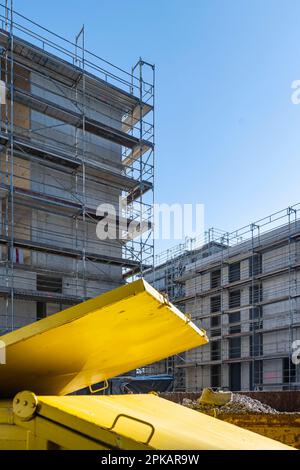 Conteneur jaune pour les supports de déchets de construction devant une coque d'échafaudage à ciel bleu Banque D'Images