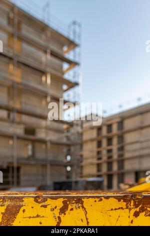 Conteneur jaune pour les supports de déchets de construction devant la coque de construction d'échafaudage avec ciel bleu au coucher du soleil Banque D'Images