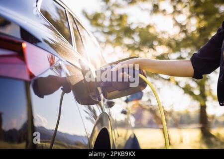 Jeune femme brancher le chargeur dans une voiture électrique noire, concept d'énergie renouvelable Banque D'Images