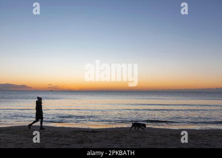 Angleterre, Dorset, Poole, Sandbanks Beach, Silhouette of Woman Walking Dog at Sunrise Banque D'Images