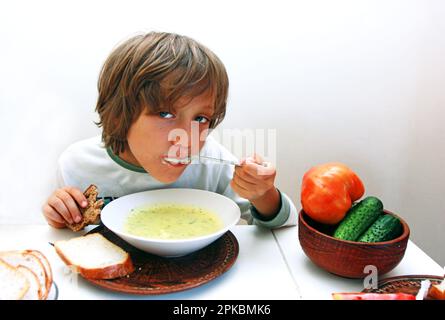 le garçon mange de la soupe de légumes avec une cuillère et du pain à la table du dîner Banque D'Images