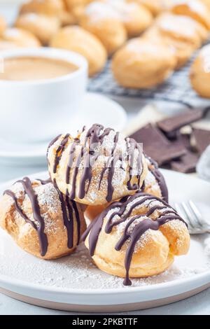 Profiteroles à la crème fouettée et au chocolat, recouverts de chocolat fondu, sur une assiette, verticale Banque D'Images