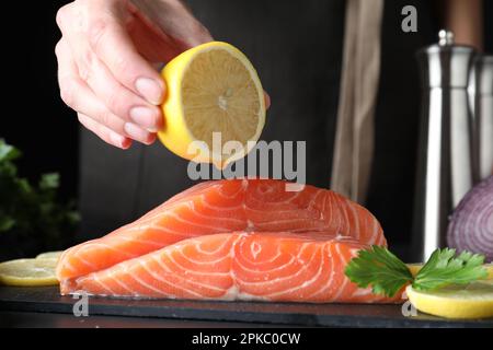 Femme pressant le citron sur le saumon frais cru à la table, gros plan. Délicatesse du poisson Banque D'Images