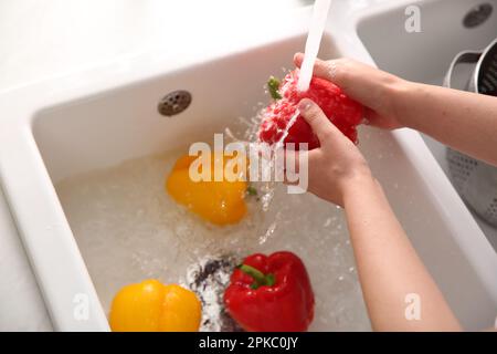 Femme lavant des poivrons frais dans l'évier de cuisine, gros plan Banque D'Images