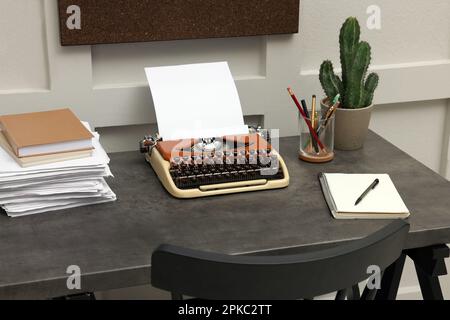 Machine à écrire et pile de papier sur table sombre dans la chambre. Lieu de travail du rédacteur Banque D'Images