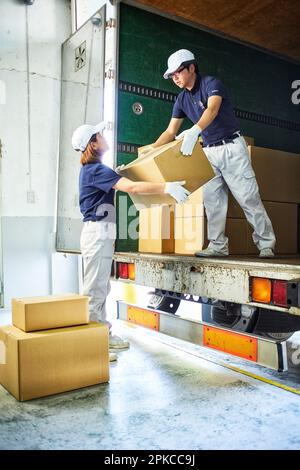 Homme et femme en vêtements de travail déchargeant des boîtes en carton du camion Banque D'Images