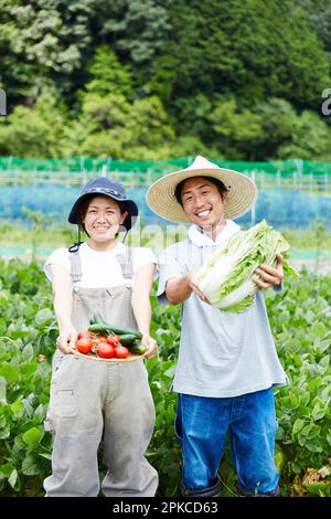 Homme et femme tenant des légumes dans un champ Banque D'Images