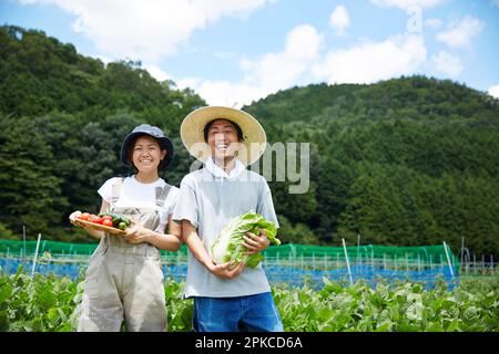 Homme et femme tenant des légumes dans un champ Banque D'Images