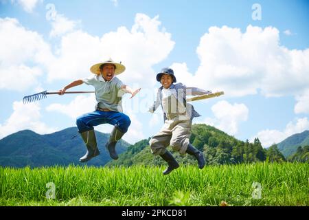 Des hommes et des femmes sautant devant un champ de paddy Banque D'Images