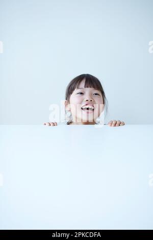 Une petite fille qui se trouve sous une table blanche Banque D'Images