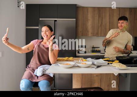 Deux jeunes latino prennent un selfie avec le téléphone tout en cuisinant. Banque D'Images