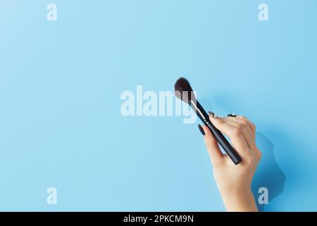 Main de femme avec brosse à poudre sur fond bleu clair Banque D'Images