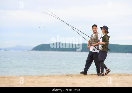 Hommes et femmes marchant sur la plage avec du matériel de pêche Banque D'Images