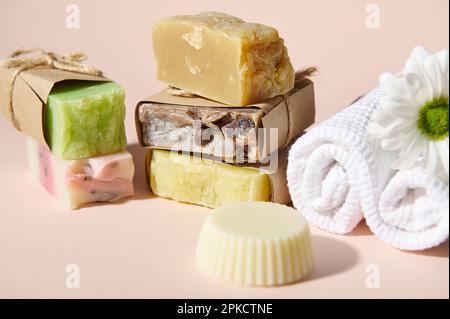 Encore la vie avec un assortiment de barres de savon naturel biologique fait main et fleur de camomille sur une serviette blanche, isolée sur rose Banque D'Images