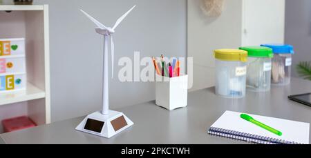 Gros plan du moulin à vent solaire et des poubelles sélectives sur le bureau dans une salle de classe environnementale vide. Concept d'éducation écologique. Banque D'Images