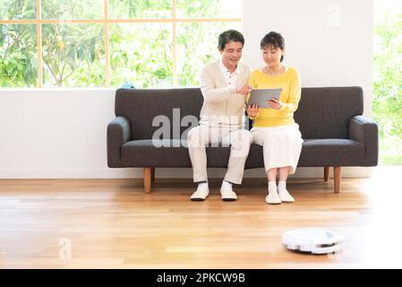 Un couple d'âge moyen regardant un PC sur un canapé avec un robot de nettoyage Banque D'Images