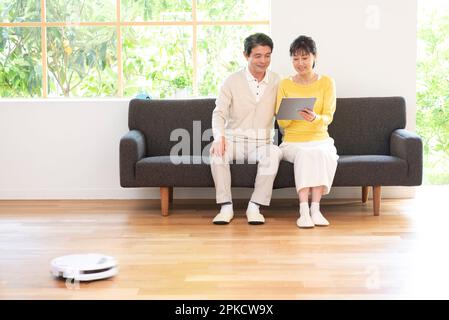 Un couple d'âge moyen regardant un PC sur un canapé avec un robot de nettoyage Banque D'Images