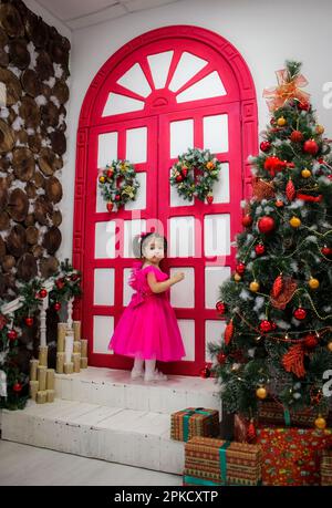 Une petite fille dans une robe rouge se tient devant des portes fermées. Banque D'Images