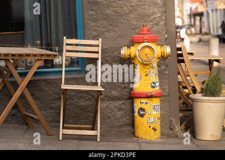 Hydrant jaune et rouge en acier emblématique avec autocollants devant un café à côté d'une table et d'une chaise extérieures à Reykjavik, en Islande. Banque D'Images