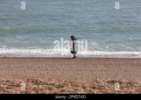 Une jeune femme marchant seule sur une plage de galets près de la mer. Banque D'Images